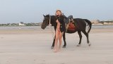 Watch adorable redhead lady riding big black horse outdoors. She is smiling happily demonstrating her natural tits and shaved pussy to the viewers.